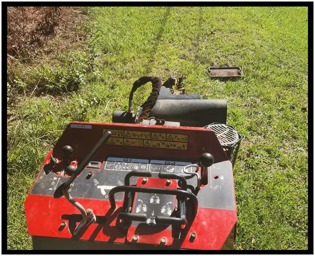 A red and black lawn mower sitting in the grass.