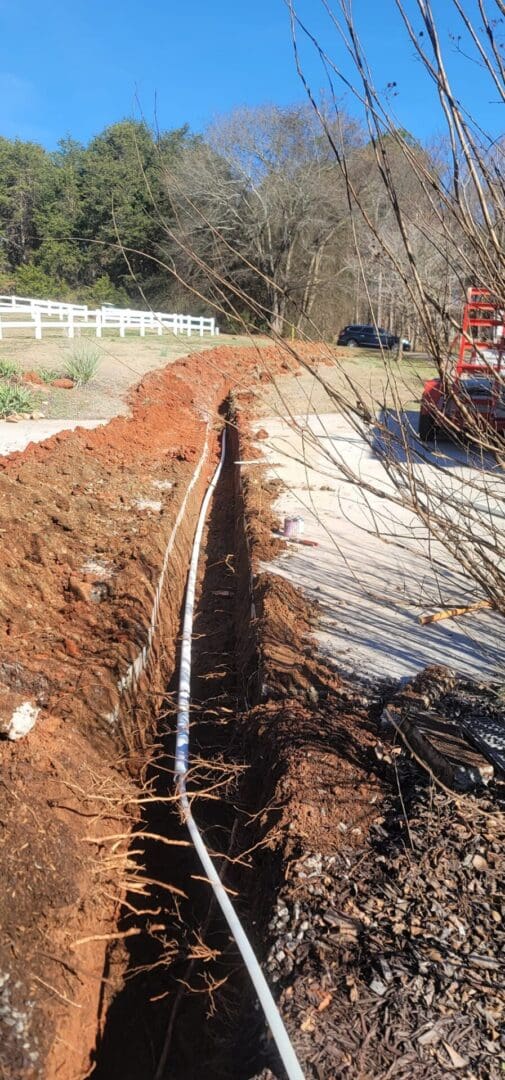 A pipe laying in the ground next to a fence.